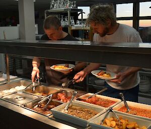 Two expeditioners serve themselves Saturday brunch cooked items from the bain marie