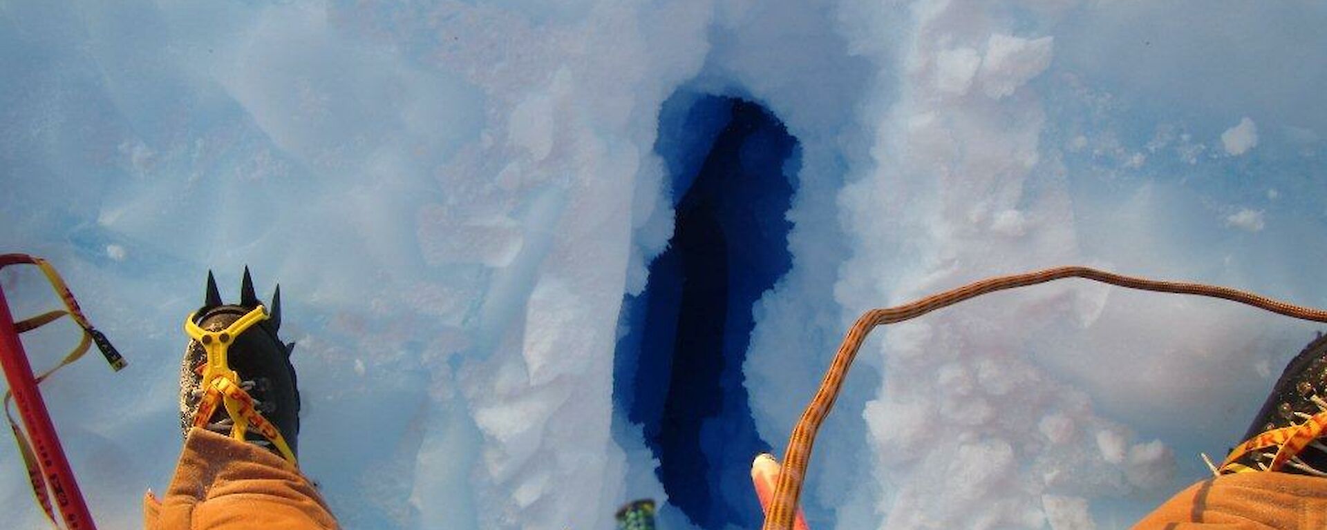 An expeditioner straddling a crevasse approximately 30cm wide and seemingly bottomless