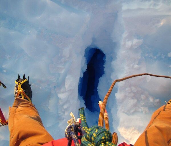 An expeditioner straddling a crevasse approximately 30cm wide and seemingly bottomless