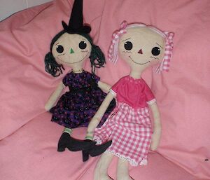 Two ragdolls — one wearing a pink checked dress and the other wearing a tall black witches hat and heels