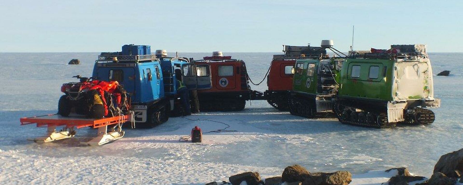 Three Hägglunds and a sled carrying a Quad motorcycle on top gathered on the plateau