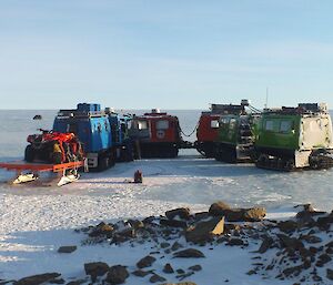 Three Hägglunds and a sled carrying a Quad motorcycle on top gathered on the plateau