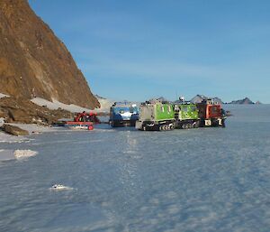 The three Hägglunds parked beneath Rumdoodle Peak with the sun shining across the plateau