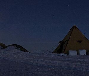 Polar tent accommodation at night with big oversnow vehicle on right and a small rocky hill on left