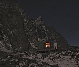 Rumdoodle hut at night with the light on inside the hut and silhouette of the mountain range behind