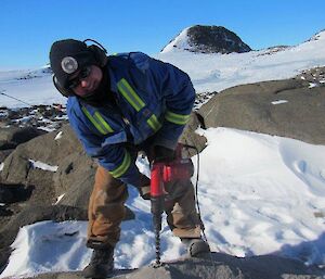 Chris smiles at the camera while drilling new anchor points into the rock for the relocation of Colbeck Hut