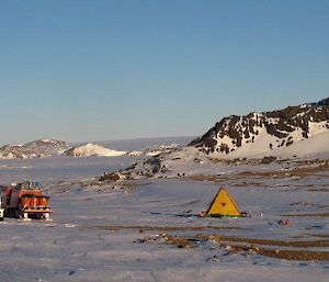 Ledinghams Depot — looking toward William Scoresby Bay with the hut on the left of frame and a polar pyramid on the right of frame settled beneath a rocky outcrop