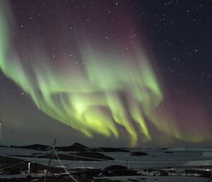An aurora dancing across the sky with a wind turbine in the foreground