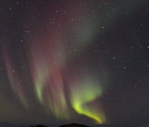 The red Macey apple hut underneath a green and pink aurora