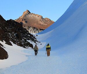 Two expeditioners walk along the side of a massive wind scour