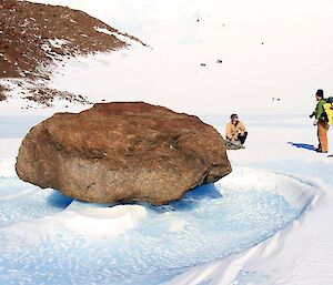 Two expeditioners stop to check out a rock caught in the frozen ice floe
