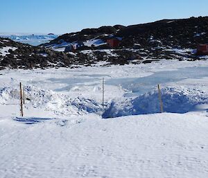 The old location in the foreground which can be seen as a hole in the ice with the new location in the distance which is slightly more elevated and perched on a rocky saddle