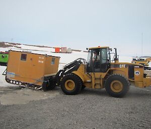 A CAT excavator with the hut lifted off the ground readys to transport the hut into the workshop