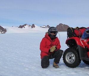 Curly crouched beside his Quad bike with the Southern Masson Ranges in the background