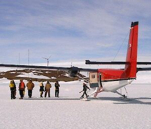 The Twin Otter arriving at Mawson Station as passengers disembark and luggage is soon to be transported to nearby vehicles