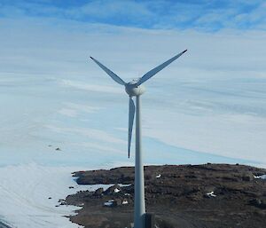 The view from the top looking toward the plateau with the wind turbine in the foreground and vehicle tracks leading away from station