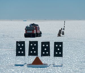 A Hägglunds oversnow vehicle looks like a toy from a distance as it sits amongst skiway flags