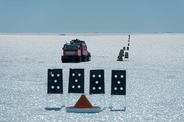 A Hägglunds oversnow vehicle looks like a toy from a distance as it sits amongst skiway flags