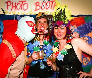 A masked man with two female expeditioners in the photo booth