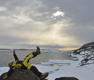 A expeditioner laying backwards on a rock with his legs in the air.