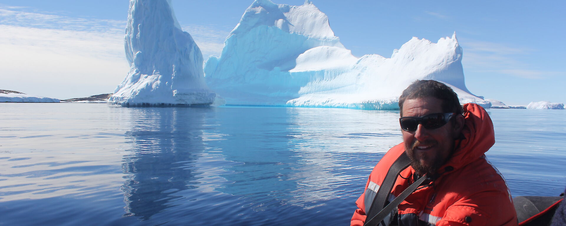 An expeditioner posing for a photo in front of an iceber