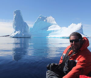 An expeditioner posing for a photo in front of an iceber