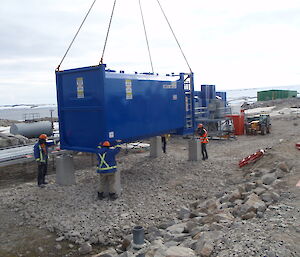 A crane lowering a new fuel tank onto the concrete pedestal legs.