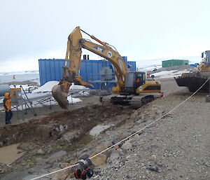 Foundations dug deeper for the new fuel tank by an excavator while a workman looks on