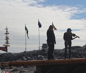 Two expeditioners standing on the back of a truck singing a the National Anthem