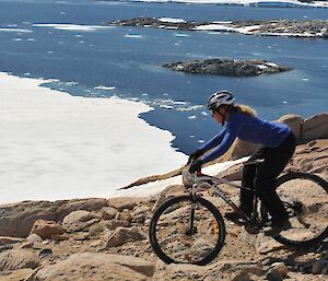 A female expeditioner riding a push bike with ice and bergs in the background
