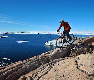 A male expeditioner on a bike with Antarctic backdrop.