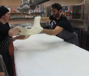 Two chefs stretching pastry for a strudel