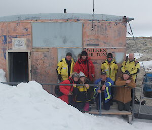Eight expeditioners pose before a field hut