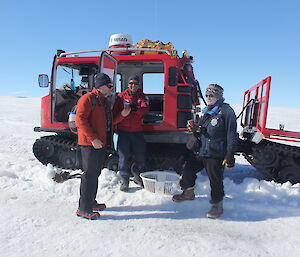 Three expeditioners standing next to a Hagglund having a drink of water