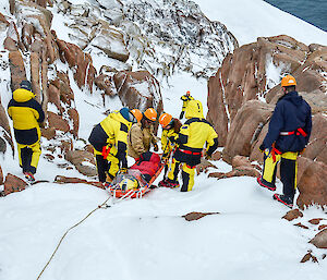 Expeditioners lowering a stretcher down a steep hill
