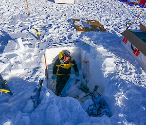 An expeditioner sitting in a large hole dug in the snow