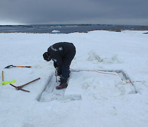 An expeditioner cutting ice with a chainsaw