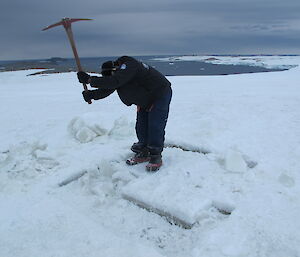 An expeditioner using a pick to smash the ice
