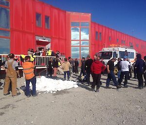 A group of people gather outside of a large accommodation facility to say farewell to departing colleagues