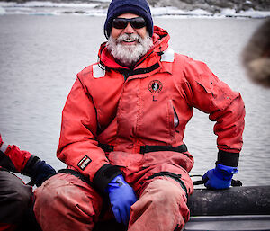 Older male expeditioner with beard and sunglasses, smiles at camera from inside an inflatable rubber boat