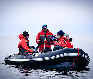 Expeditioners on an inflatable rubber boat, one smiling towards the camera