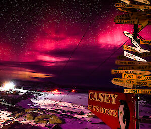 Casey station is seen from its wooden sign, with stars and aurora lighting up the night sky