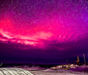 An unusually coloured aurora lights up the night sky, looking like a large alien ship is just behind the clouds