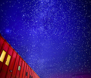 The red shed accommodation building at night, with thousands of stars in the sky and odd light created by an aurora australis