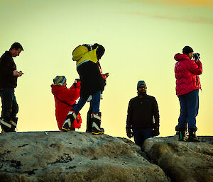 Expeditioners take photos of sunset from a rocky perch