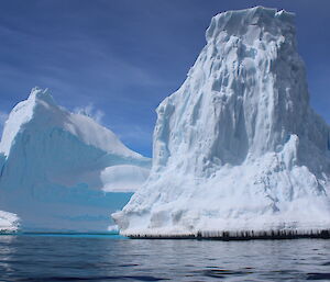 Two large, tall icebergs on a sunny day, taken from a small boat