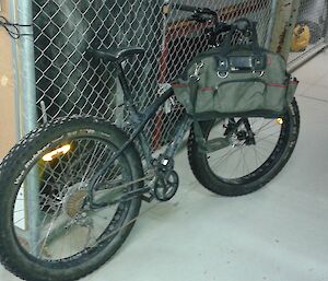 Plumber’s bike with saddle bag leans up against chain link fence inside warehouse