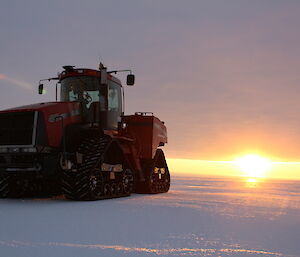 A large tracked vehicle sits on the ice while the sun sets in the distance