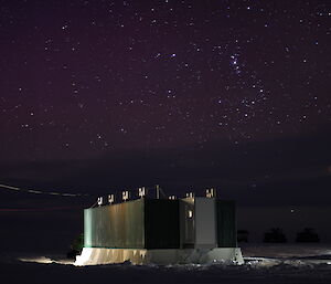 A shipping container accommodation module with lights at night, the sky filled with stars