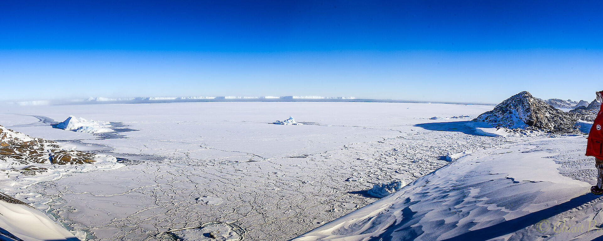 An expeditioner dressed in red winter gear looks across the vast white Vanderford Glacier